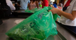 Pessoa embala compras em um saco verde que remete à nova lei de sacolas plásticas