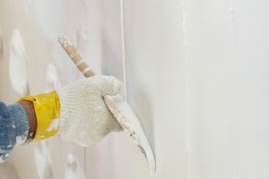 Mão com luva aplica rejunte e argamassa na parede