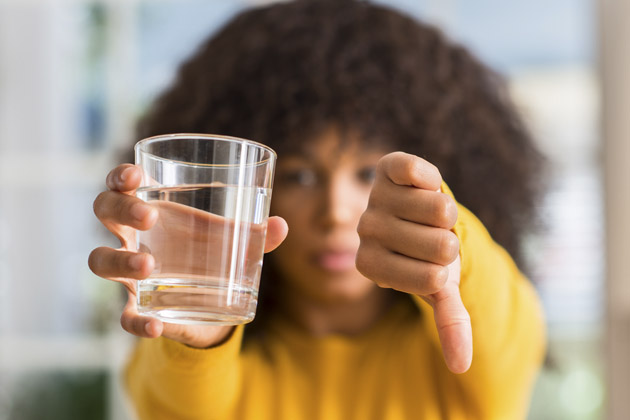 Mulher fazendo sinal de negativo ao segurar um copo d'água, indicando que o líquido está ruim