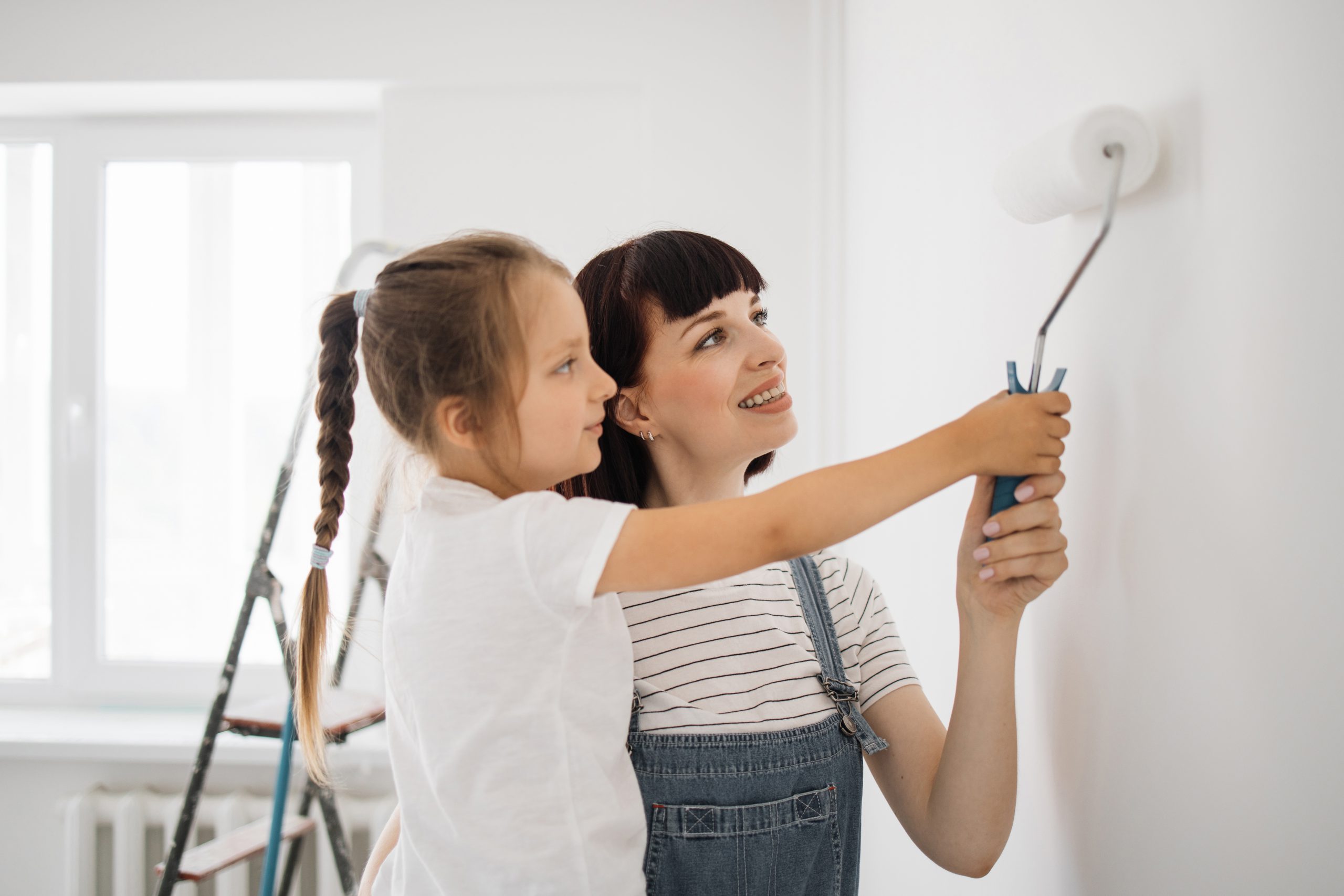 Happy Family Mother And Daughter Paint The Wall With White Paint.