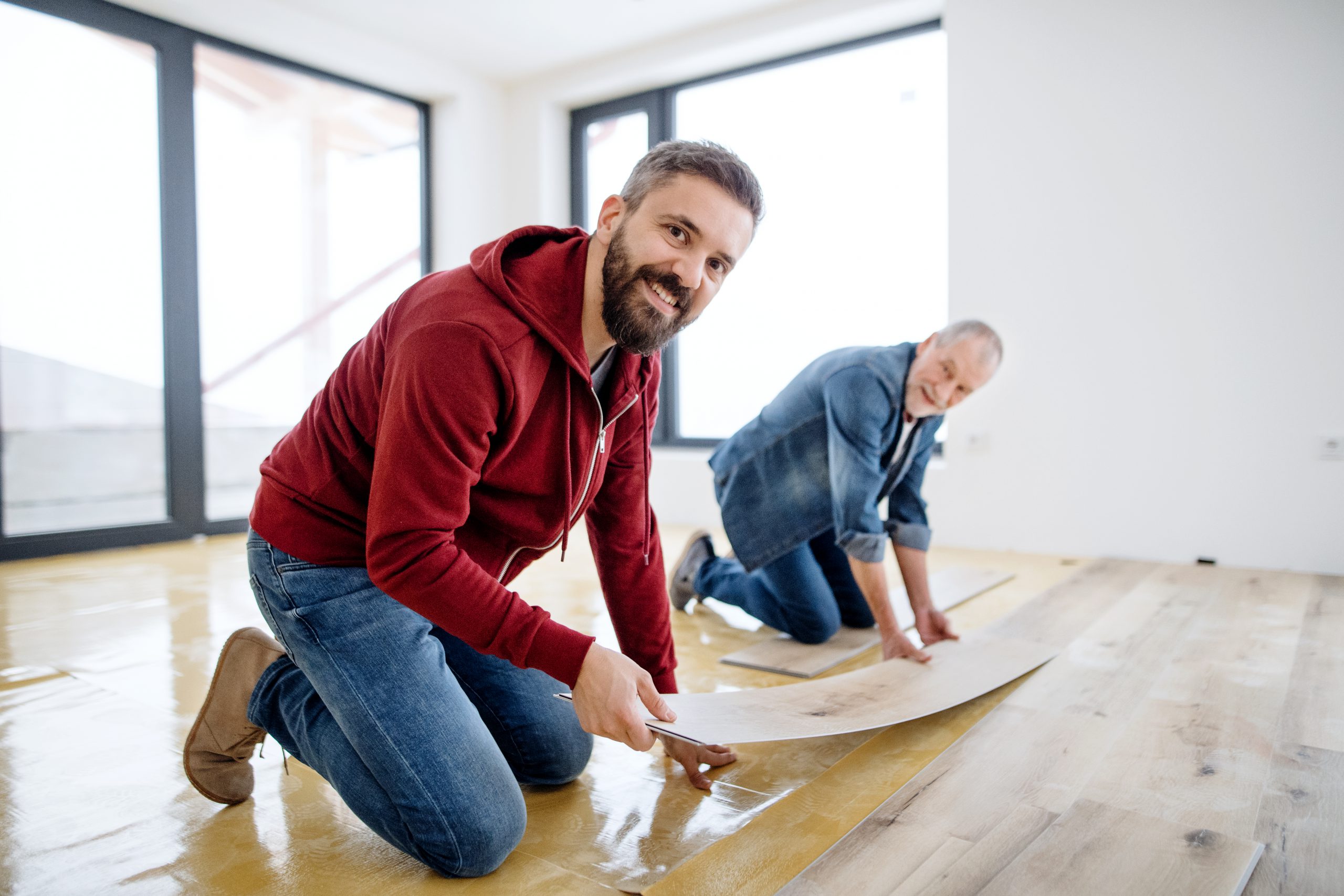 A Mature Man With His Senior Father Laying Vinyl Flooring, A New Home Concept.