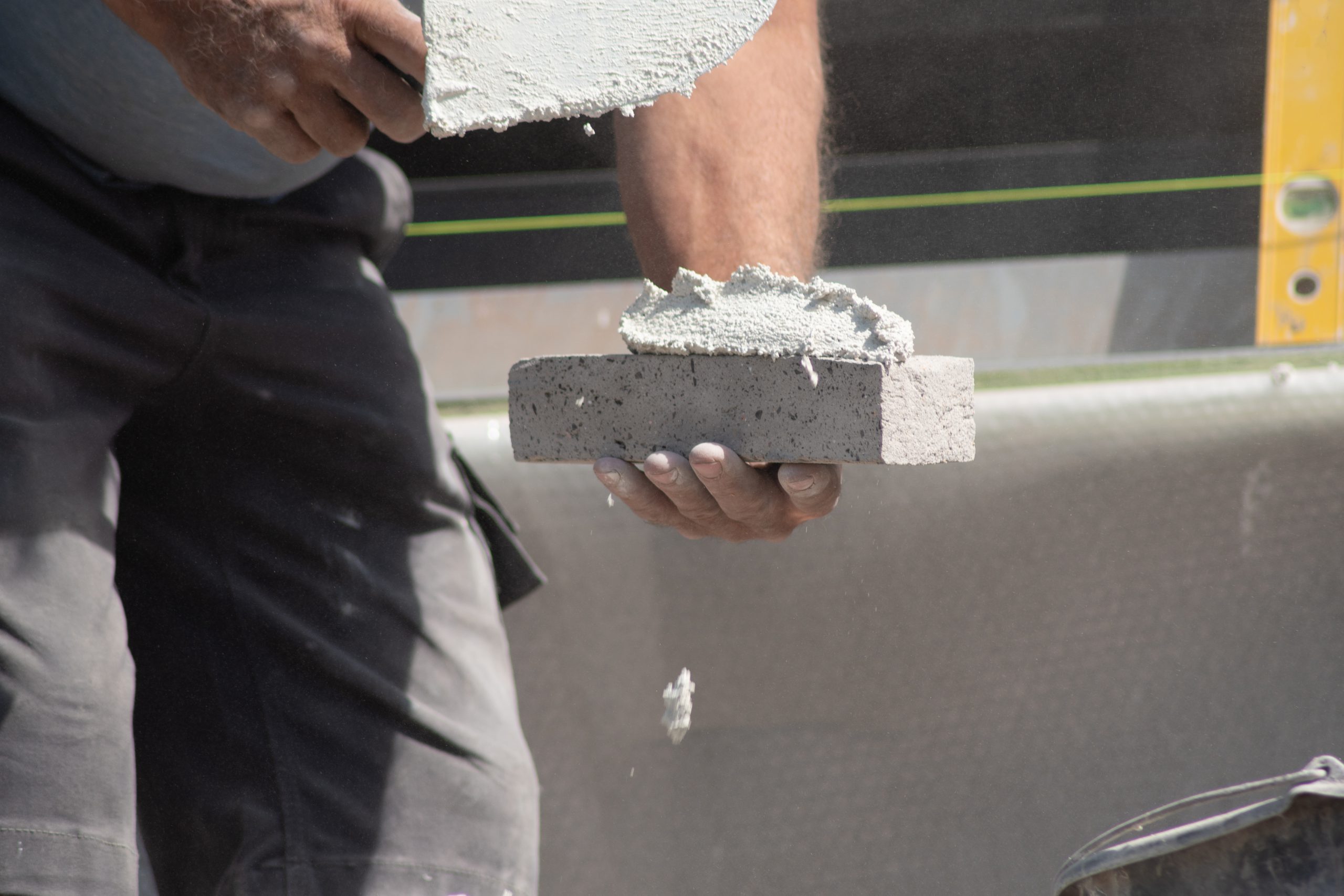 Close Up Of The Hands Of A Bricklayer Applying Cement Mortar To A Brick