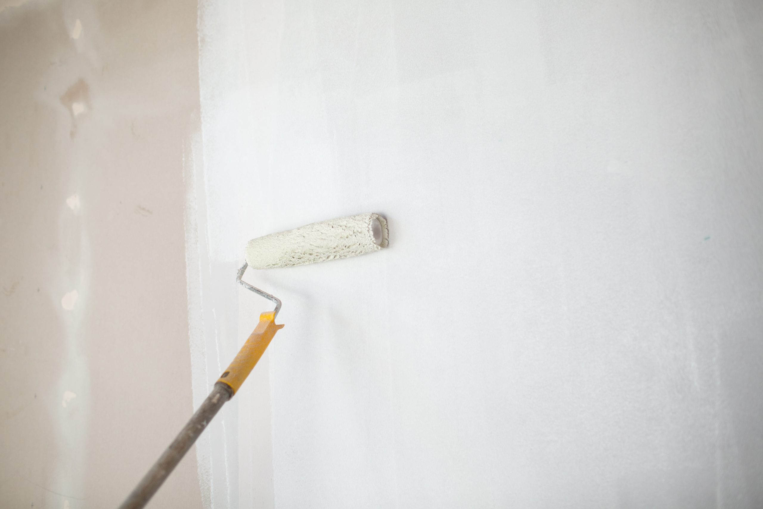 White Paint Roller In Hand With Drywall Wall Painting