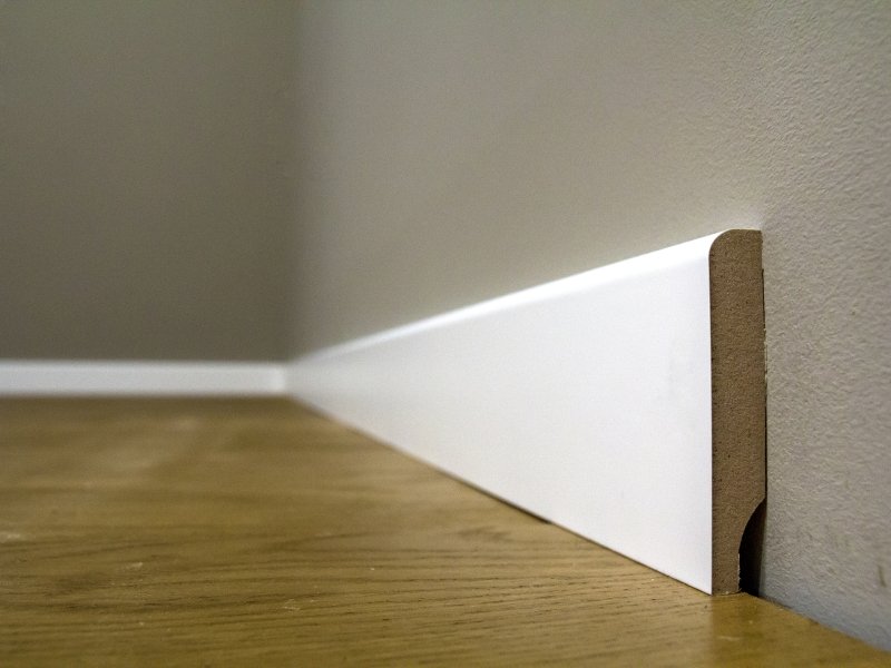 Wooden Or Plastic White Floor Plinth Installation In Big Empty Room On Wooden Floor And White Plastered Stucco Walls Background. Interior Details.